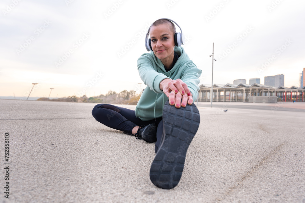 Sporty woman with sports headphones doing stretching sitting concentrated looking at camera.