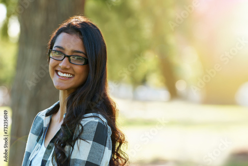 Woman, portrait and relaxing in park or garden, smiling and joyful on summer holiday. Female person, eyewear and enjoying vacation in countryside, outdoors and calm student on weekend in nature