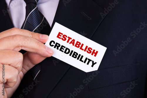 Businessman putting a card with text establish credibility in the pocket