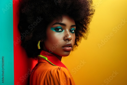 A young woman with a striking jheri curl and vibrant makeup poses against a wall, her doll-like features and bold lip capturing the eye in this indoor setting