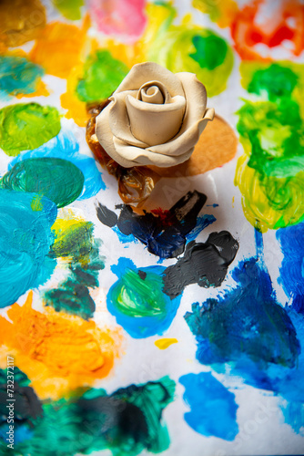 White rose on the background of a multicolored palette of paints