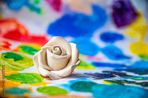 White rose on the background of a multicolored palette of paints