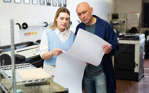 Service engineer and office worker checking printed document together against color chart