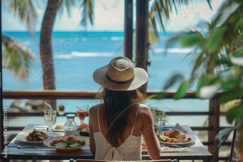 A woman eats food and enjoys the ocean view. Tropical vacation dining table. The concept of travel © Kien