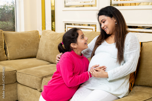 Happy indian woman expecting a baby daughter touching her belly while sitting on couch. healthcare concept