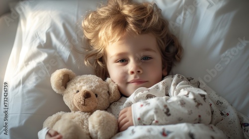 A young child with blonde hair wearing pajamas lying in bed with a teddy bear.