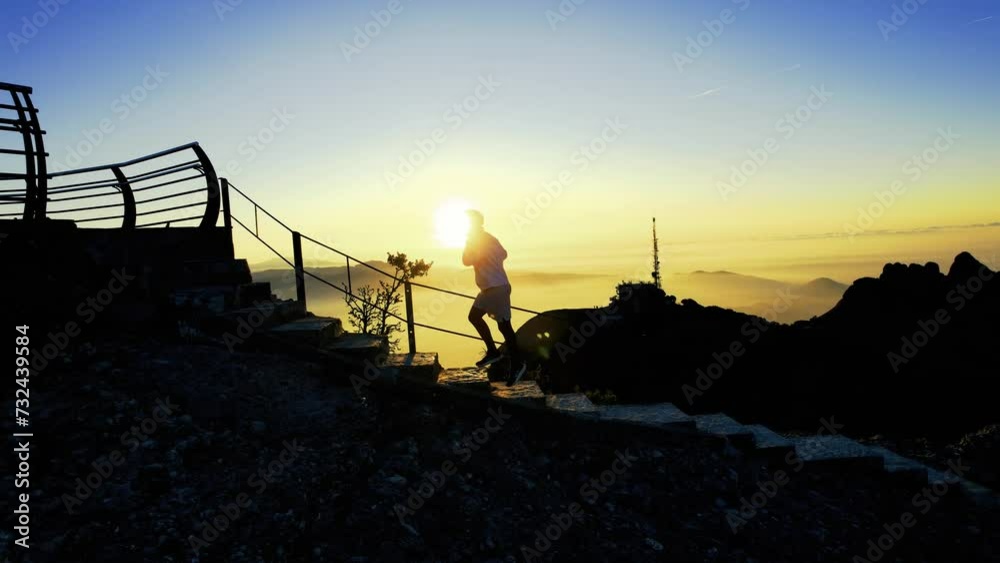 Silueta de deportista ascendiendo montaña con escalones al amanecer con la salida del sol detrás por encima de las nubes