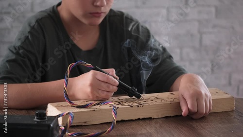 Teenager artist drawing on a wooden plank with a pyrograph.  photo