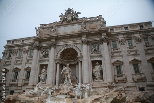 Large Trevi Fountain adorns the exterior of a modern building, its features illuminated by the sun