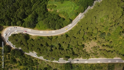 Aerial view of a winding road ascends a steep hill with a picturesque forest