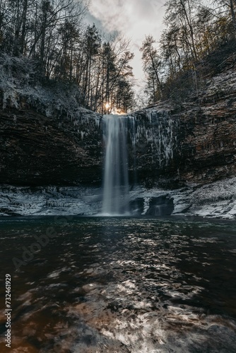 Vertical shot of a waterfall cascading down between large frozen rocks