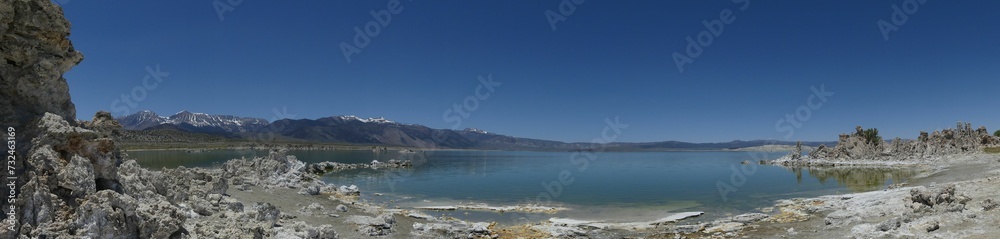Scenic, panoramic view of a calm lake with a rocky shoreline surrounded by mountains in the distance
