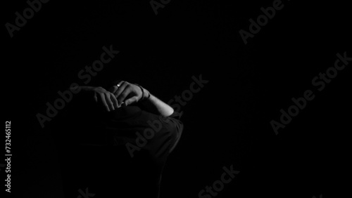 Grayscale shot of a man standing alone in a dark setting, his arms resting atop his head.