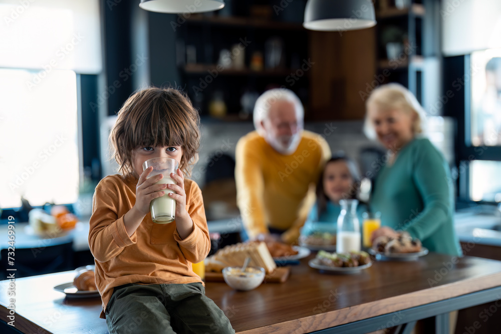 Portrait of a cute boy drinking milk from a glass while sitting on the table during breakfast with sister and grandparents. Portrait of a cute boy drinking milk from a glass while sitting on the table during breakfast with sister and grandparents.