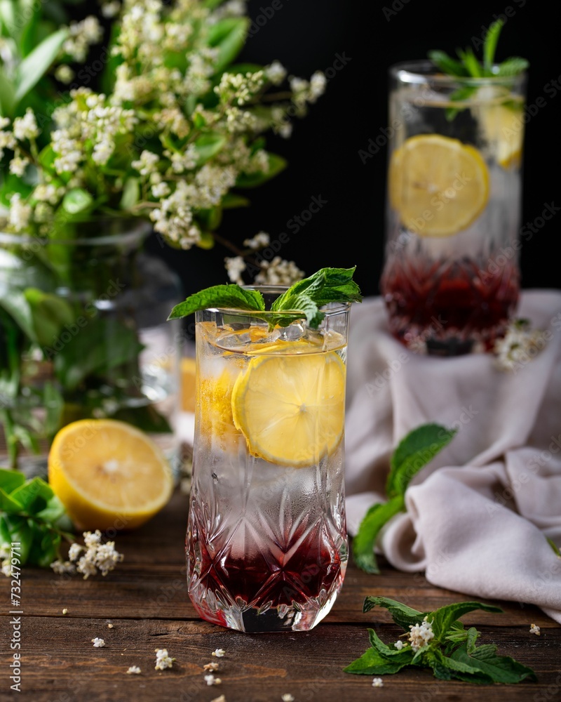 Glass of refreshing lemonade garnished with fresh lemons and mint leaves, set on a wooden table Glass of refreshing lemonade garnished with fresh lemons and mint leaves, set on a wooden table