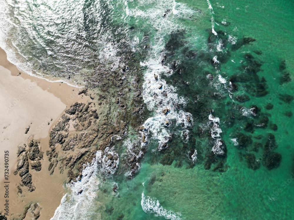 Aerial shot of a stunning beach with small rocks and stones near foamy waves