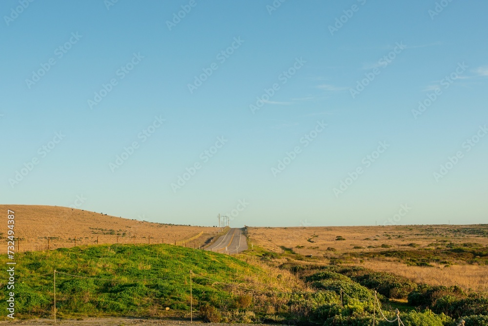 Scenic dirt road leading down a grassy hillside with a beautiful horizon in the background Scenic dirt road leading down a grassy hillside with a beautiful horizon in the background