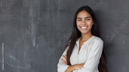 Portrait of a young latin woman with pleasant smile and crossed arms isolated on grey wall with copy space. Beautiful girl with folded arms looking at camera against grey wall - generative ai