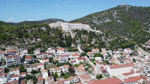 Drone footage over traditional town houses under green ridge and Fortica Fortress in Hvar, Croatia photo