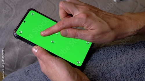 Woman Hand Holding Smartphone with Green Screen in Room at Bedtime. Fingers touch the touch screen, dial a password, number, or code. Chroma key layout for copy space. Unlocking your mobile phone. photo