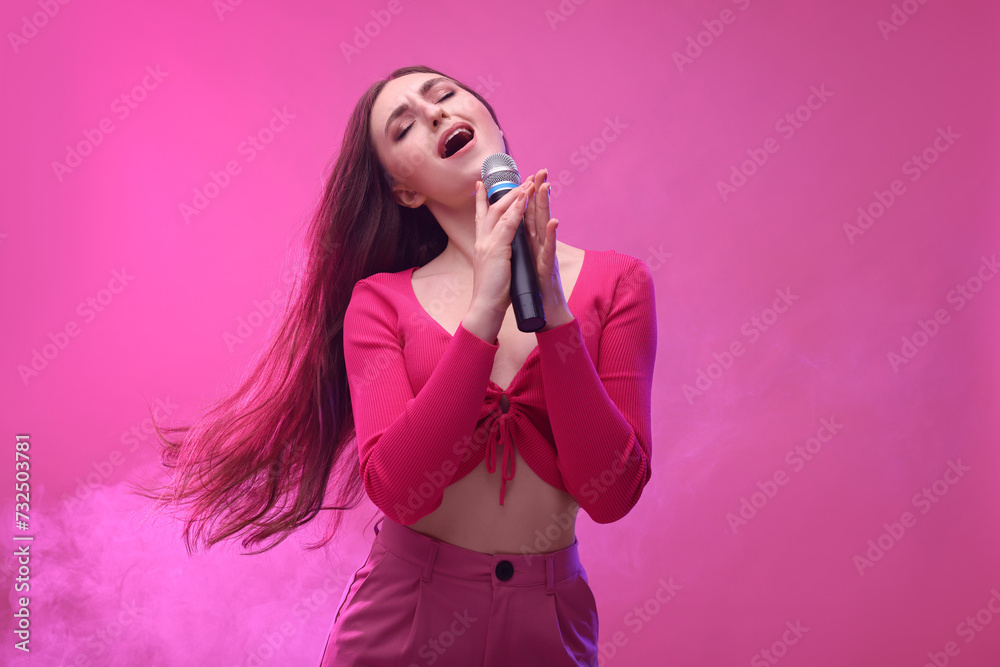 Emotional woman with microphone singing on pink background
