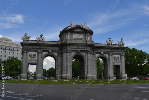 an arch in front of the tall buildings and grass and trees