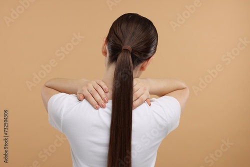 Woman touching her neck on beige background, back view