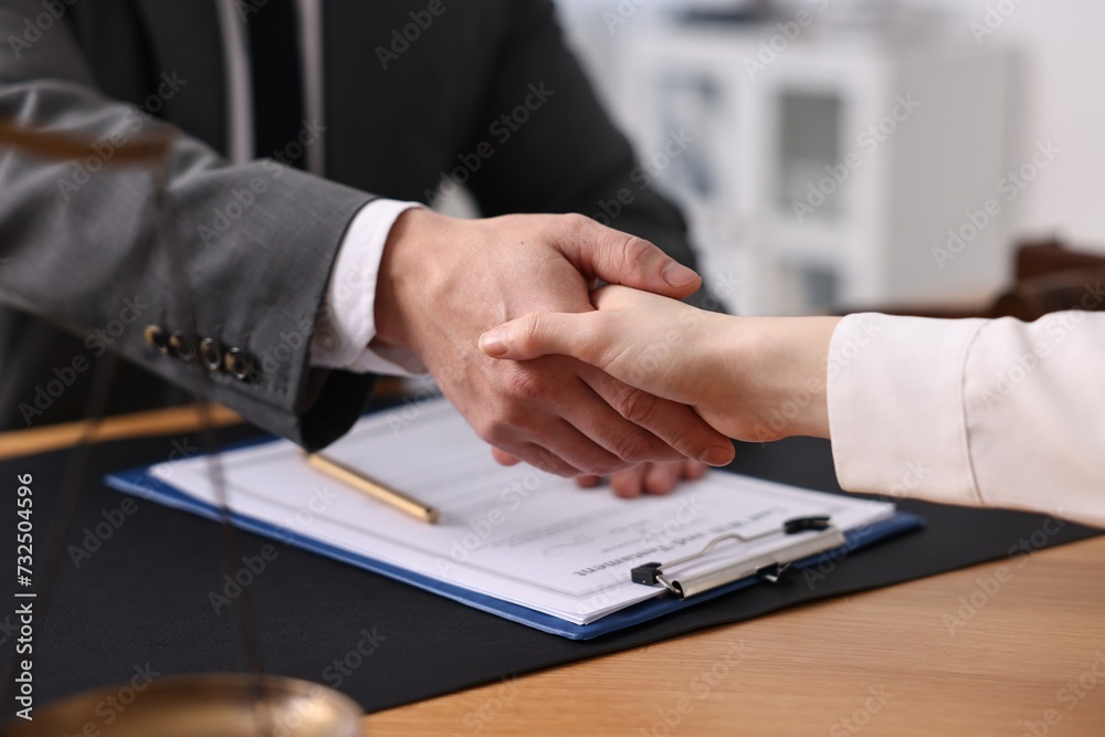 Fototapeta premium Notary shaking hands with client at wooden table in office, closeup