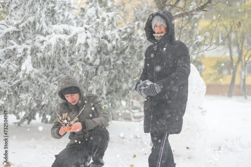 a girl and a boy is playing with snow on the street, making snowman, it is snowing, a blizzard and frost on a winter day