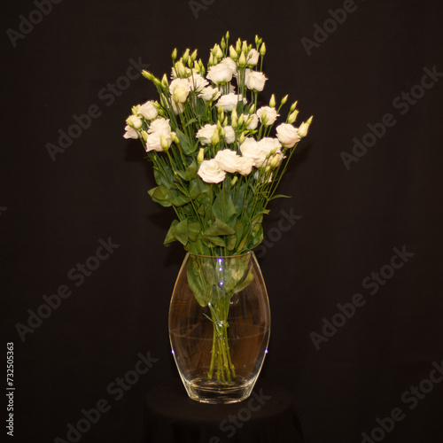 Glass vase filled with a vibrant bouquet of red flowers on a black background