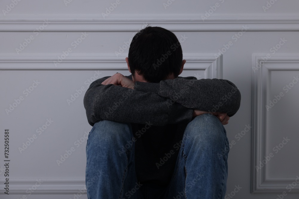 Sad man sitting near white wall indoors