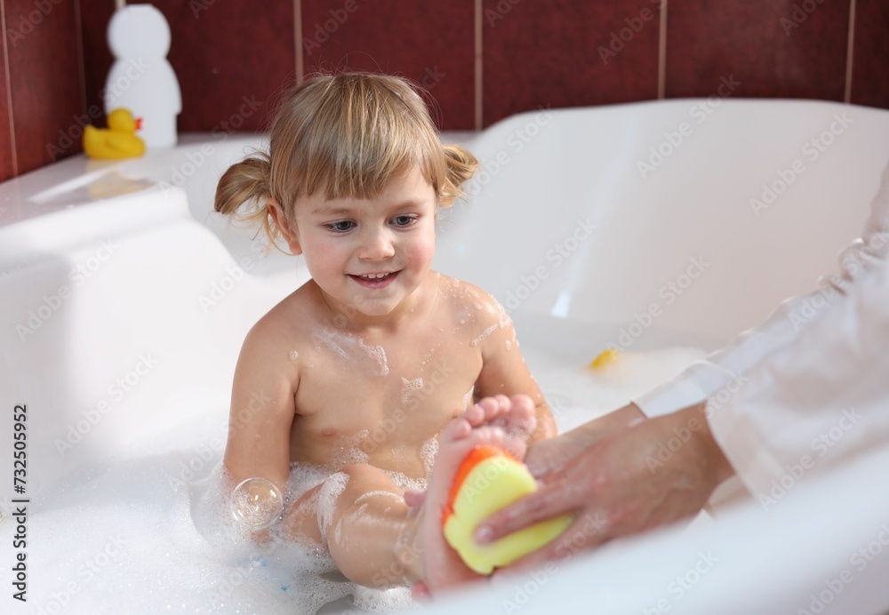 Mother washing her smiling daughter with sponge in bathtub, closeup Mother washing her smiling daughter with sponge in bathtub, closeup