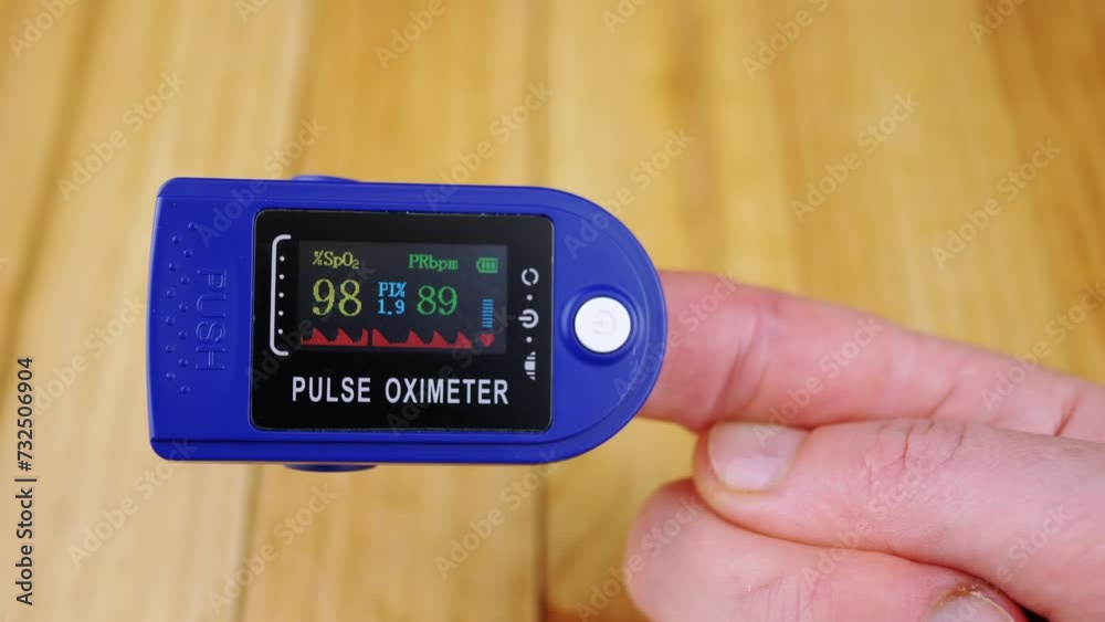 Woman Measures Pulse and Oxygen Saturation Using a Pulse Oximeter at Home. Close-up. Wooden background. A dial with sensors and indicators on the device. Measurement of heart rate, pulse, heartbeat. Woman Measures Pulse and Oxygen Saturation Using a Pulse Oximeter at Home. Close-up. Wooden background. A dial with sensors and indicators on the device. Measurement of heart rate, pulse, heartbeat.