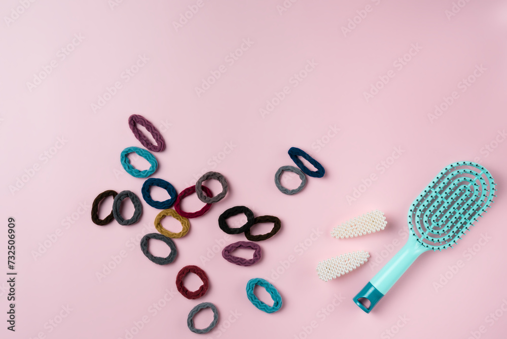 Blue hairbrush with lots of hair ties on a pink background. - obrazy, fototapety, plakaty 