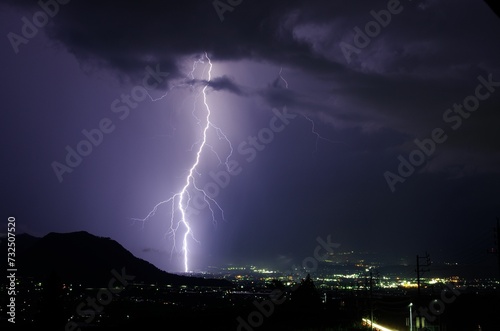Night sky illuminated with a dazzling display of purple lightning bolts against a city skyline