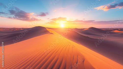 The sun dips below the horizon, casting a warm glow over smooth sand dunes in a vast desert landscape.  © Oranuch