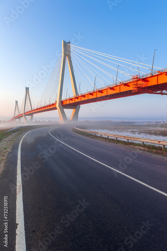 Cable-stayed bridge in fog, in the light of the morning sun and against the background of a clear blue sky. Murom. Russia.