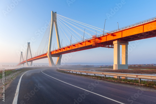 Cable-stayed bridge in fog, in the light of the morning sun and against the background of a clear blue sky. Murom. Russia.