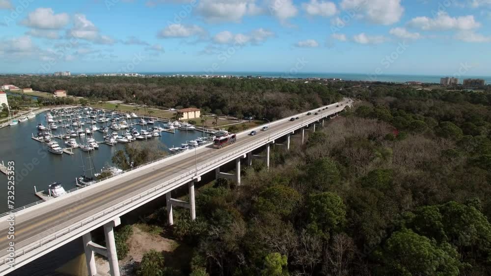 Aerial Shot Of Rv Bus Moving On Seabreeze Bridge By Nautical Vessels At Harbor In Sea, Drone Flying Backwards On Sunny Day - Daytona Beach , Florida Aerial Shot Of Rv Bus Moving On Seabreeze Bridge By Nautical Vessels At Harbor In Sea, Drone Flying Backwards On Sunny Day - Daytona Beach , Florida