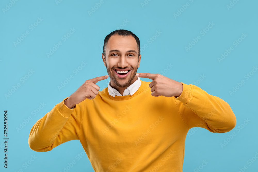 Smiling man pointing at his healthy clean teeth on light blue background Smiling man pointing at his healthy clean teeth on light blue background