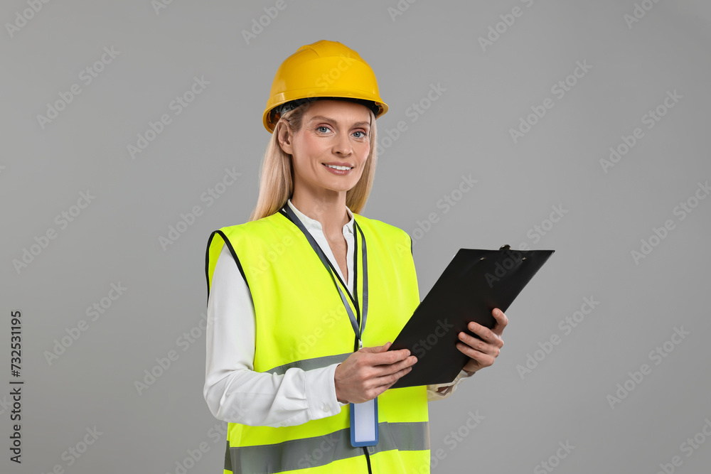 Engineer in hard hat holding clipboard on grey background Engineer in hard hat holding clipboard on grey background