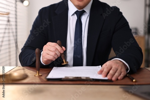 Notary stamping document at wooden table in office, closeup