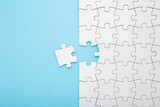 Unfinished white puzzle with last one piece on light blue table background. Pastel color. Closeup. Top down view.