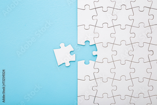 Obraz na plátně Unfinished white puzzle with last one piece on light blue table background