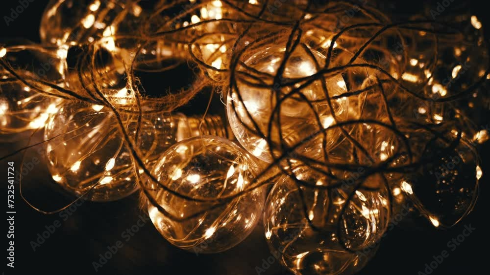 Glowing Garland of Glass Light Bulbs with Dim Yellow Light in a Dark Room. Close up. Texture. Bunch. Christmas decorations with retro style hanging electric lights illuminating the space. Design.