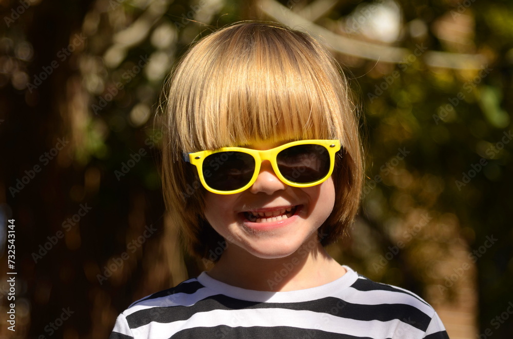 Portrait of a cute boy with long hair wearing sunglasses. Concept: happy childhood, advertising for a kindergarten. Portrait of a cute boy with long hair wearing sunglasses. Concept: happy childhood, advertising for a kindergarten.