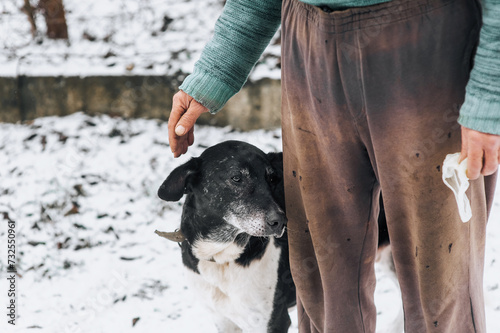 An elderly homeless man, an old man caresses his hand on the head of an old big sad hungry mongrel dog with scars in the winter on the snow outdoors. Close-up photograph of an animal with a person.