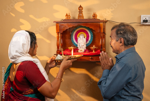 Devotional Indian woman giving aarthi to husband after offering to god at home - concept of spirituality, mindfulness and Hinduism. photo