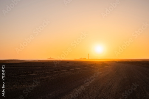 Carretera infinita de la arena con el sol de fondo a punto de esconderse por el horizonte