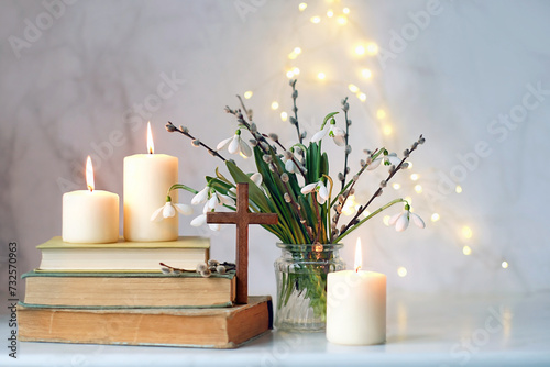 christian cross, religion books, candles and bouquet with Snowdrop flowers on table, abstract light background. Religious church holiday. symbol of faith in God, Easter, Palm Sunday